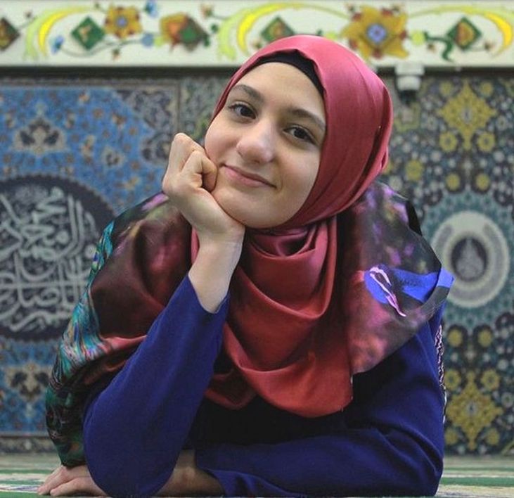 Fotografia de Fatima usando veu vermelho e diante de uma parede ornamentada com azulejos